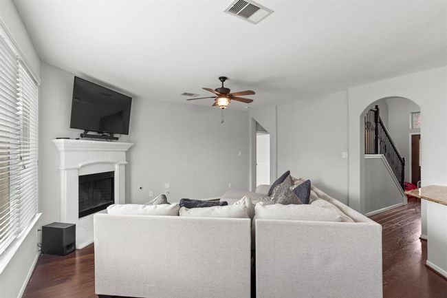 Walk through the foyer past the staircase and arrive at this incredible living room! Beautiful views of the backyard are provided by the incredible windows with privacy blinds. It is highlighted by a gorgeous fireplace, wood floors, and a ceiling fan. | Image 9