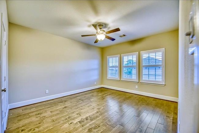 This room features hardwood flooring, neutral walls, and a ceiling fan. It has three large windows with plantation shutters, offering plenty of natural light. | Image 40