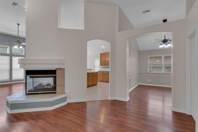 Unfurnished living room featuring ceiling fan, arched walkways, a fireplace, wood finished floors, and high vaulted ceiling | Image 11