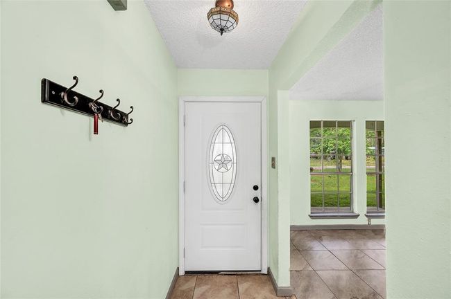 Welcome home through this charming entryway, featuring elegant tile flooring, a stylish coat rack, and abundant natural light from adjacent windows. | Image 12