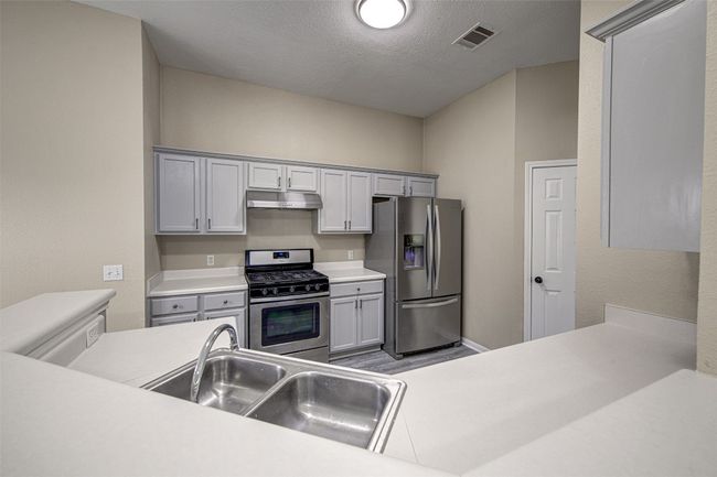 Kitchen with appliances with stainless steel finishes, under cabinet range hood, light countertops, a textured ceiling, and gray cabinets | Image 7