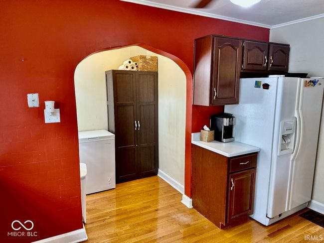 kitchen with white refrigerator with ice dispenser, arched walkways, light countertops, light wood-style flooring, and ornamental molding | Image 22