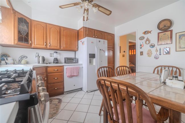 Kitchen with white appliances, glass insert cabinets, light tile patterned flooring, brown cabinetry, and ceiling fan | Image 6
