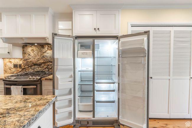 Kitchen featuring light stone counters, appliances with stainless steel finishes, white cabinetry, backsplash, and ornamental molding | Image 9