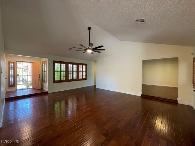 Unfurnished living room with ceiling fan, vaulted ceiling, dark wood-type flooring, plenty of natural light, and a textured ceiling | Image 10