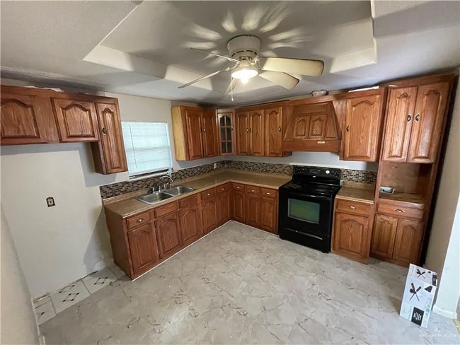 Kitchen featuring black / electric stove, a sink, brown cabinets, and a tray ceiling | Image 10
