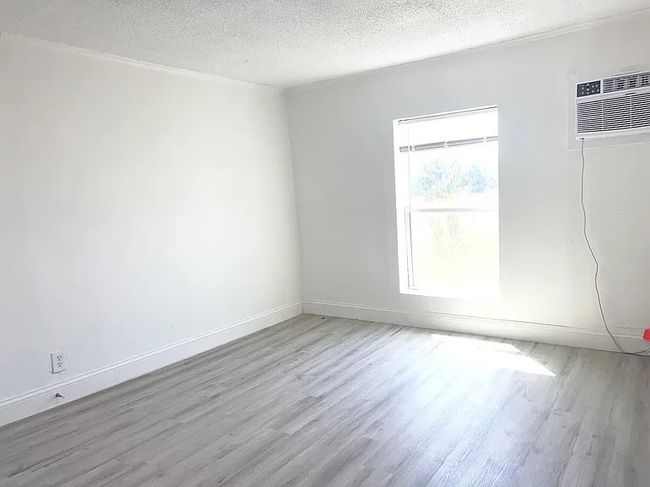 Empty room with wood finished floors, a textured ceiling, and a wall mounted AC | Image 5