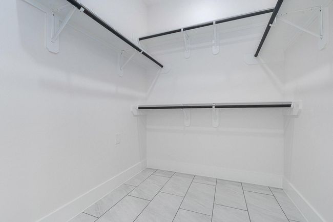 This is a spacious walk-in closet with multiple shelves and hanging rods, featuring sleek white walls and tiled flooring, ideal for organized storage. | Image 26