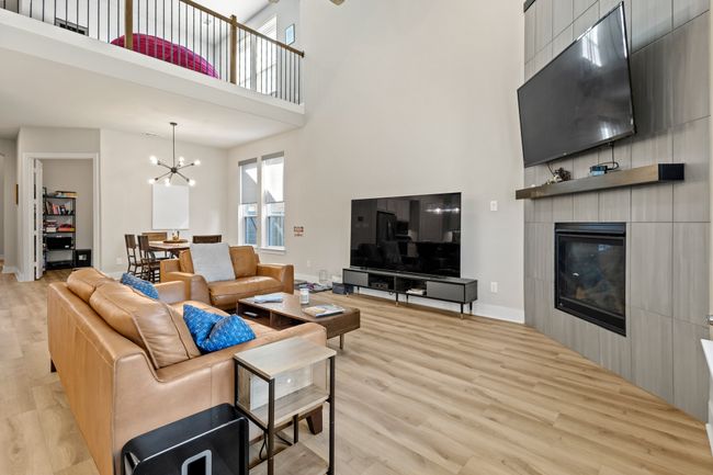 Living room with light wood finished floors, a fireplace, an inviting chandelier, and a towering ceiling | Image 5