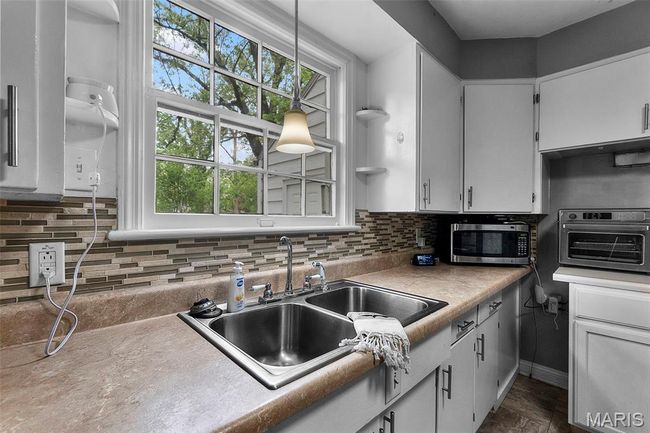 Kitchen featuring tasteful backsplash, a sink, light countertops, stainless steel microwave, and white cabinetry | Image 10