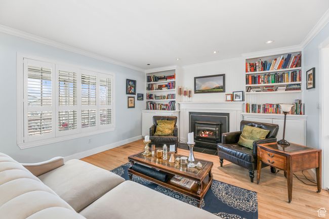 Living room with crown molding, built in features, wood finished floors, and a fireplace with flush hearth | Image 6