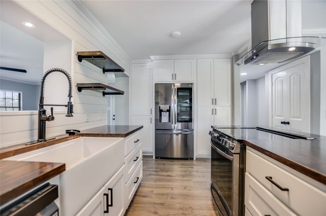 Kitchen featuring appliances with stainless steel finishes, island range hood, light wood finished floors, white cabinets, and wood counters | Image 12
