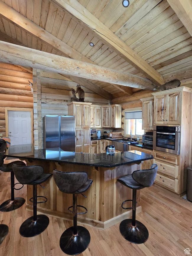 Kitchen featuring beam ceiling, a kitchen breakfast bar, appliances with stainless steel finishes, light wood-style floors, and log walls | Image 53