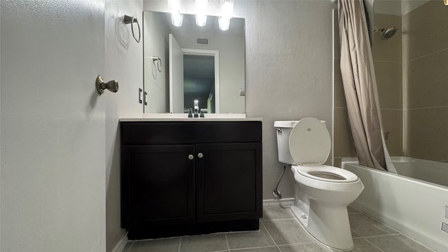 Bathroom with tile patterned floors, shower / bath combination with curtain, vanity, toilet, and baseboards | Image 14
