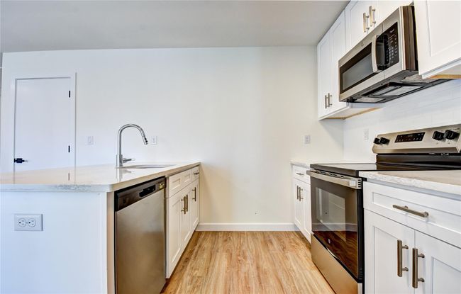 Kitchen featuring light wood finished floors, light stone counters, a peninsula, stainless steel appliances, and a sink | Image 34