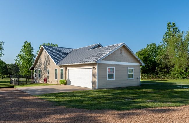 View of side of home with concrete driveway, a garage, metal roof, and a lawn | Image 4