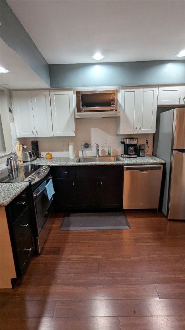 Kitchen with stainless steel appliances, a sink, white cabinets, recessed lighting, and dark wood-style floors | Image 15