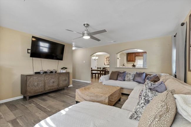 Living room featuring arched walkways, visible vents, wood finished floors, baseboards, and ceiling fan with notable chandelier | Image 13