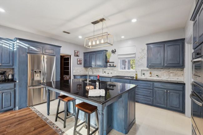 Kitchen featuring stainless steel appliances, a kitchen bar, dark stone counters, backsplash, and a center island with sink | Image 16