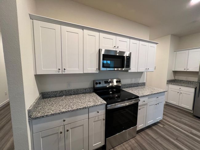 Kitchen featuring stainless steel appliances, dark wood finished floors, light stone counters, and white cabinetry | Image 4