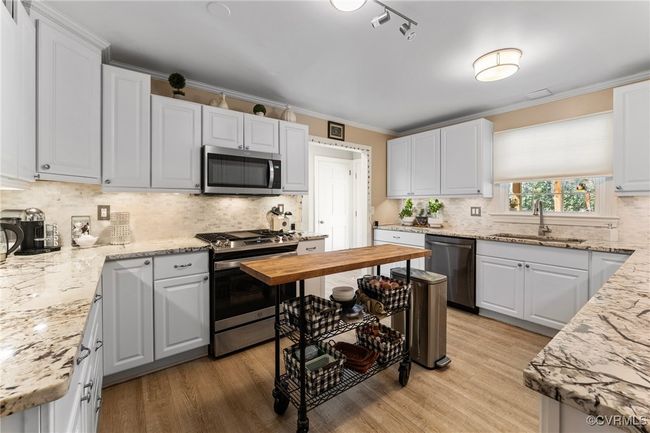 Kitchen with crown molding, decorative backsplash, light wood-style flooring, appliances with stainless steel finishes, and a sink | Image 20