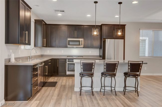 Kitchen featuring appliances with stainless steel finishes, a sink, dark brown cabinets, light wood-style flooring, and a breakfast bar area | Image 17