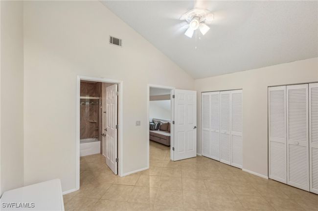 Unfurnished bedroom with multiple closets, ensuite bathroom, high vaulted ceiling, a ceiling fan, and light tile patterned floors | Image 25