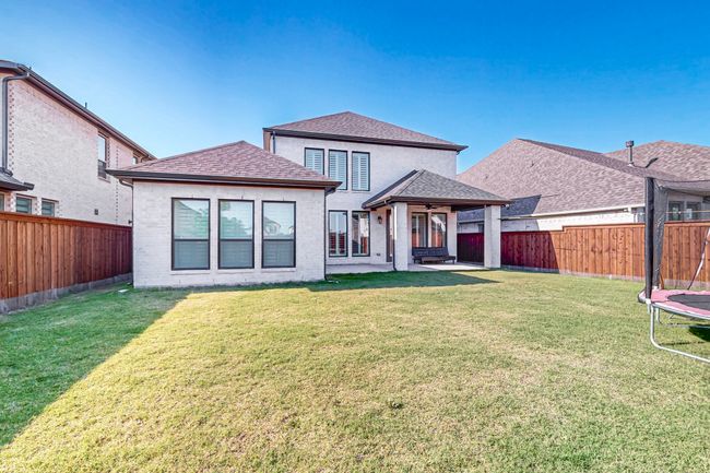 Rear view of house with a trampoline, a patio area, ceiling fan, roof with shingles, and brick siding | Image 38