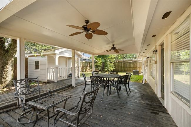 The expansive covered back deck features two ceiling fans and a storage building, with black decking and a crisp white cover that echo the home’s interior palette—a quiet, functional outdoor extension of the living space. | Image 17