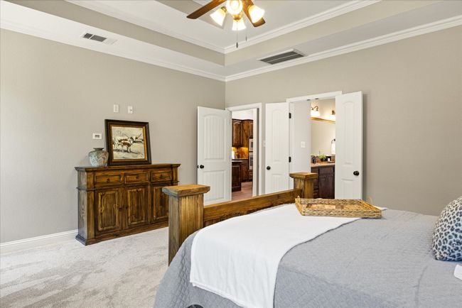 Bedroom with ornamental molding, light colored carpet, a tray ceiling, and a ceiling fan | Image 22
