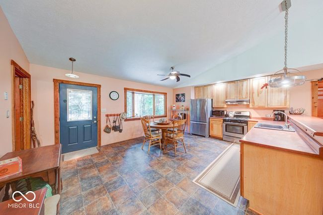kitchen with stainless steel appliances, stone finish floors, light brown cabinetry, decorative light fixtures, and lofted ceiling | Image 47