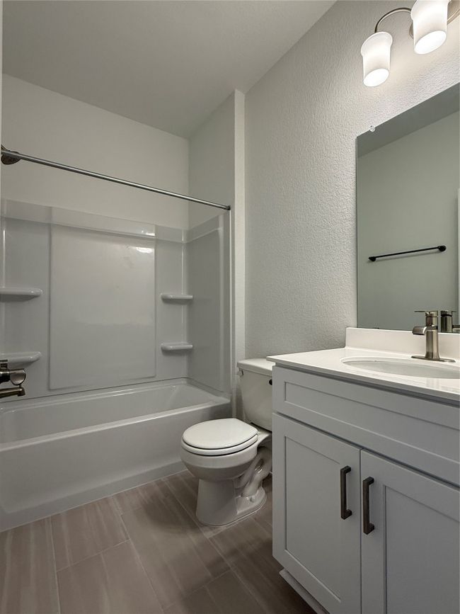 Bathroom featuring a textured wall, vanity, toilet, shower / washtub combination, and wood finished floors | Image 7