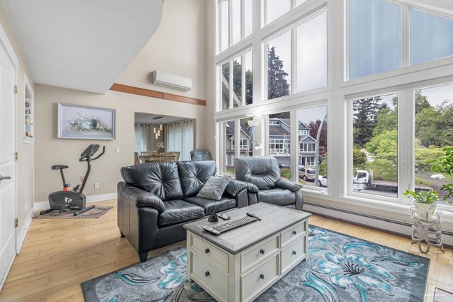 Living area with a wall mounted AC, wood-type flooring, a high ceiling, baseboards, and baseboard heating | Image 9