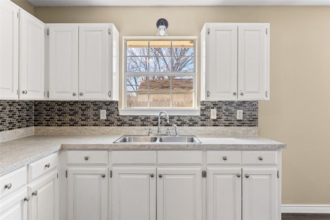 Kitchen with tasteful backsplash, white cabinets, light countertops, and a sink | Image 33