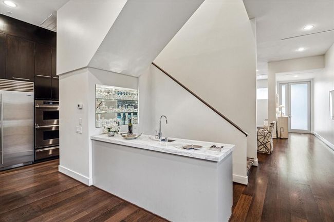 A closer look of the WET BAR with its marble slab counter, deep stainless sink, display glass shelving with mirror backing, built-in soft-close cabinets/drawers, Scotsman ice-maker, wide plank hardwood flooring. | Image 13