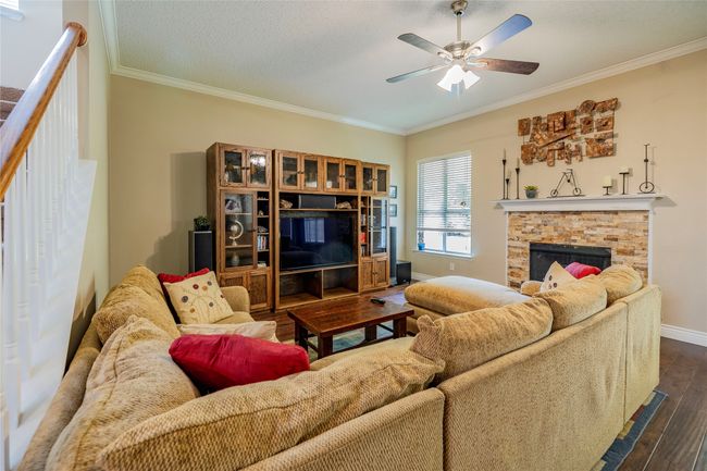 Living room with crown molding, a ceiling fan, dark wood finished floors, baseboards, and a stone fireplace | Image 12