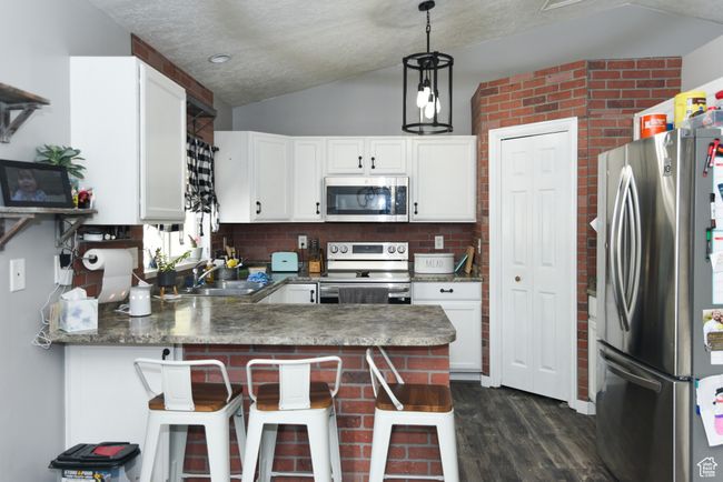 Kitchen featuring appliances with stainless steel finishes, vaulted ceiling, a sink, a peninsula, and dark wood-type flooring | Image 13