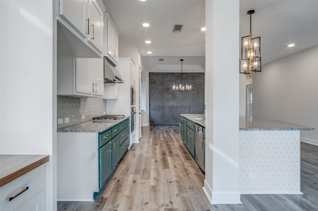 Kitchen with a chandelier, under cabinet range hood, white cabinetry, light wood-style flooring, and light stone countertops | Image 14