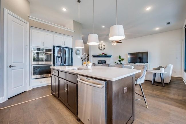 Kitchen with appliances with stainless steel finishes, a sink, a glass covered fireplace, light countertops, and dark wood finished floors | Image 18