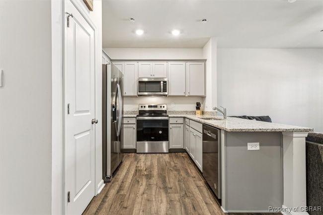 Kitchen featuring dark wood-style floors, stainless steel appliances, a sink, light stone countertops, and a peninsula | Image 6