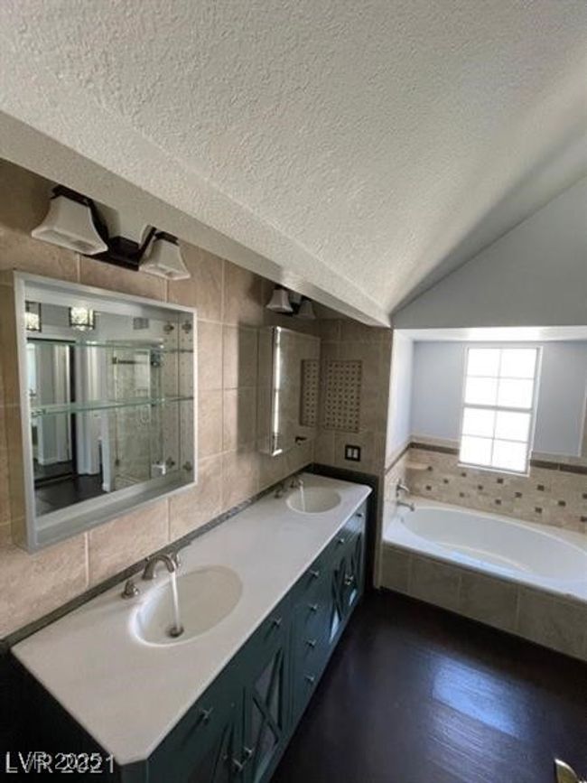 Full bath featuring a bath, a textured ceiling, double vanity, a sink, and vaulted ceiling | Image 12
