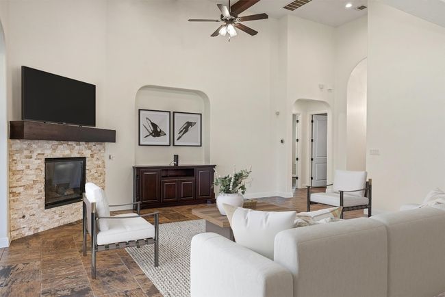 Virtually staged. Living area with a towering ceiling, a stone fireplace, a ceiling fan, dark stone finish flooring, and arched walkways | Image 4