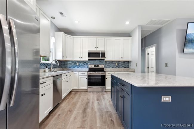 Kitchen featuring appliances with stainless steel finishes, a sink, light wood finished floors, blue cabinets, and backsplash | Image 13
