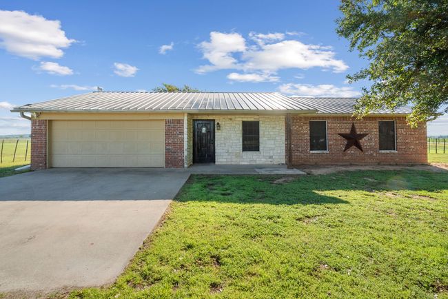 Ranch-style home featuring a garage, a metal roof, driveway, and a front lawn | Image 4