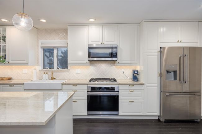 Kitchen with light stone counters, white cabinetry, stainless steel appliances, and a sink | Image 17