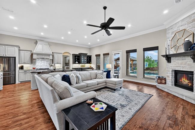 Living area with a stone fireplace, a ceiling fan, recessed lighting, light wood finished floors, and crown molding | Image 7