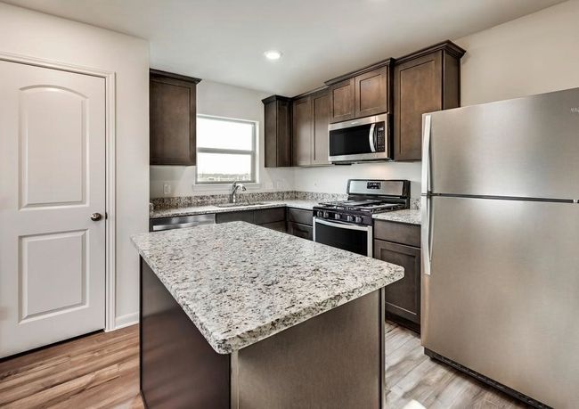 Kitchen featuring light stone counters, dark brown cabinets, appliances with stainless steel finishes, light wood-type flooring, and a center island | Image 4