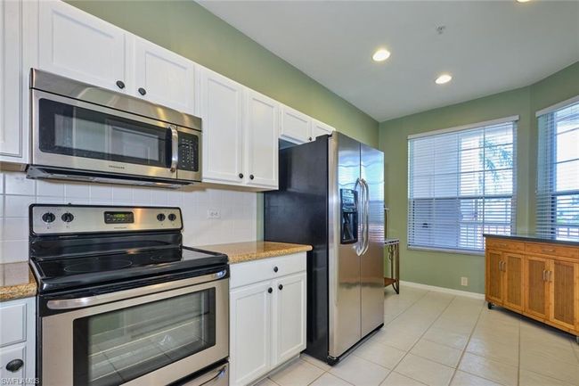 Kitchen with white cabinetry, light tile patterned flooring, backsplash, and stainless steel appliances | Image 21