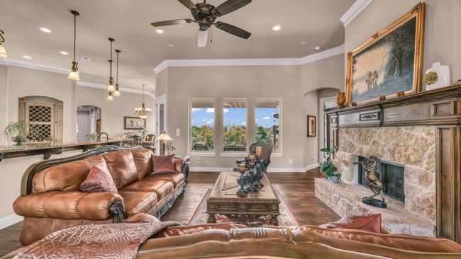 Living area with arched walkways, a stone fireplace, ceiling fan with notable chandelier, and dark wood-type flooring | Image 9