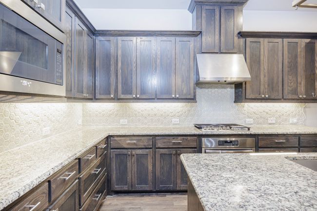 Kitchen with appliances with stainless steel finishes, exhaust hood, dark brown cabinets, and decorative backsplash | Image 22